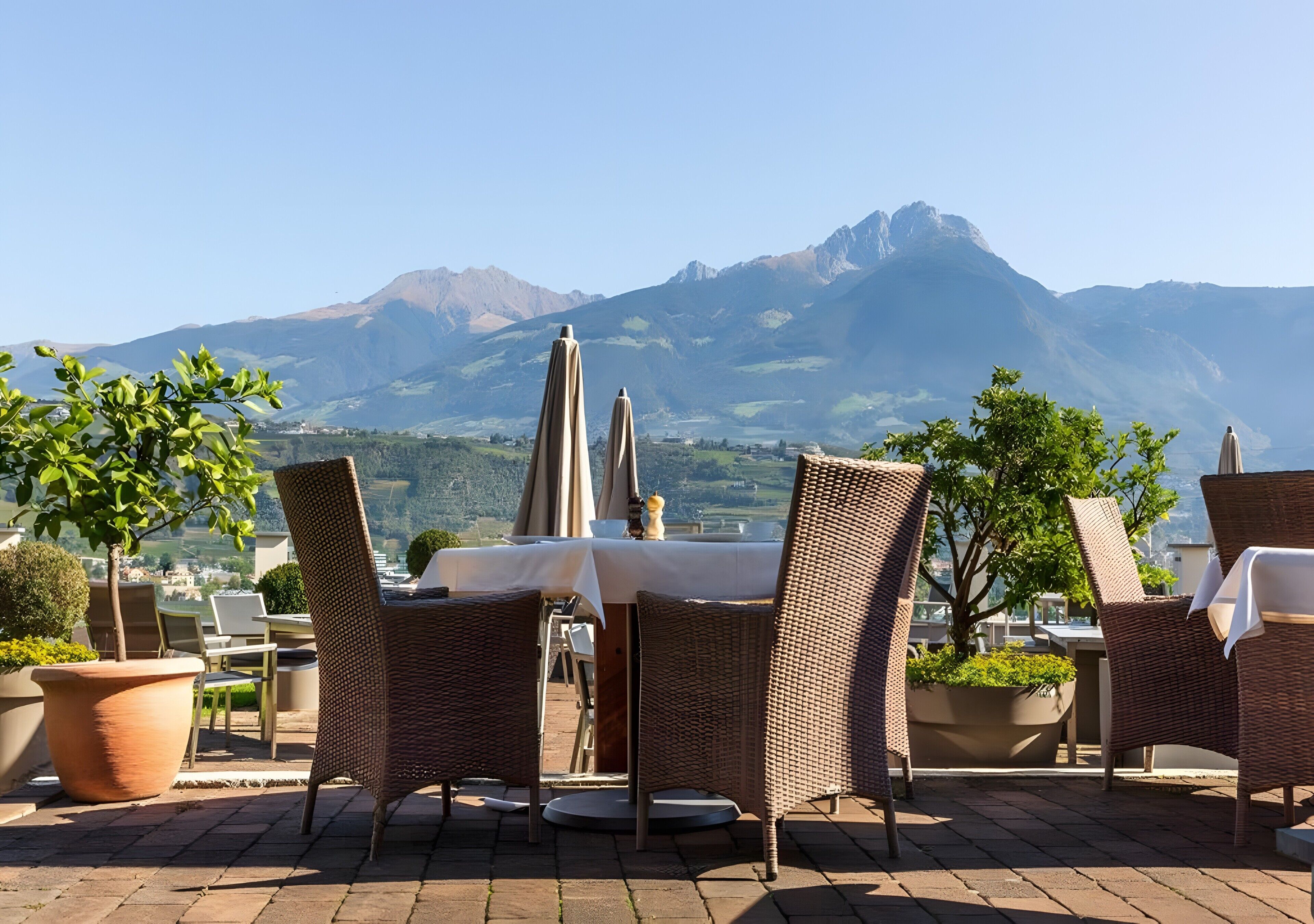 Un área de comedor al aire libre con sillas de mimbre y una mesa, con vistas a un paisaje montañoso.