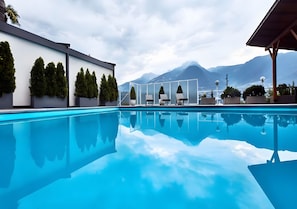 Une piscine avec vue sur les montagnes, des chaises longues et une façade de bâtiment moderne.