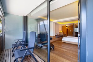 A modern room with a glass wall, a bed, a sofa, and a seating area with chairs.