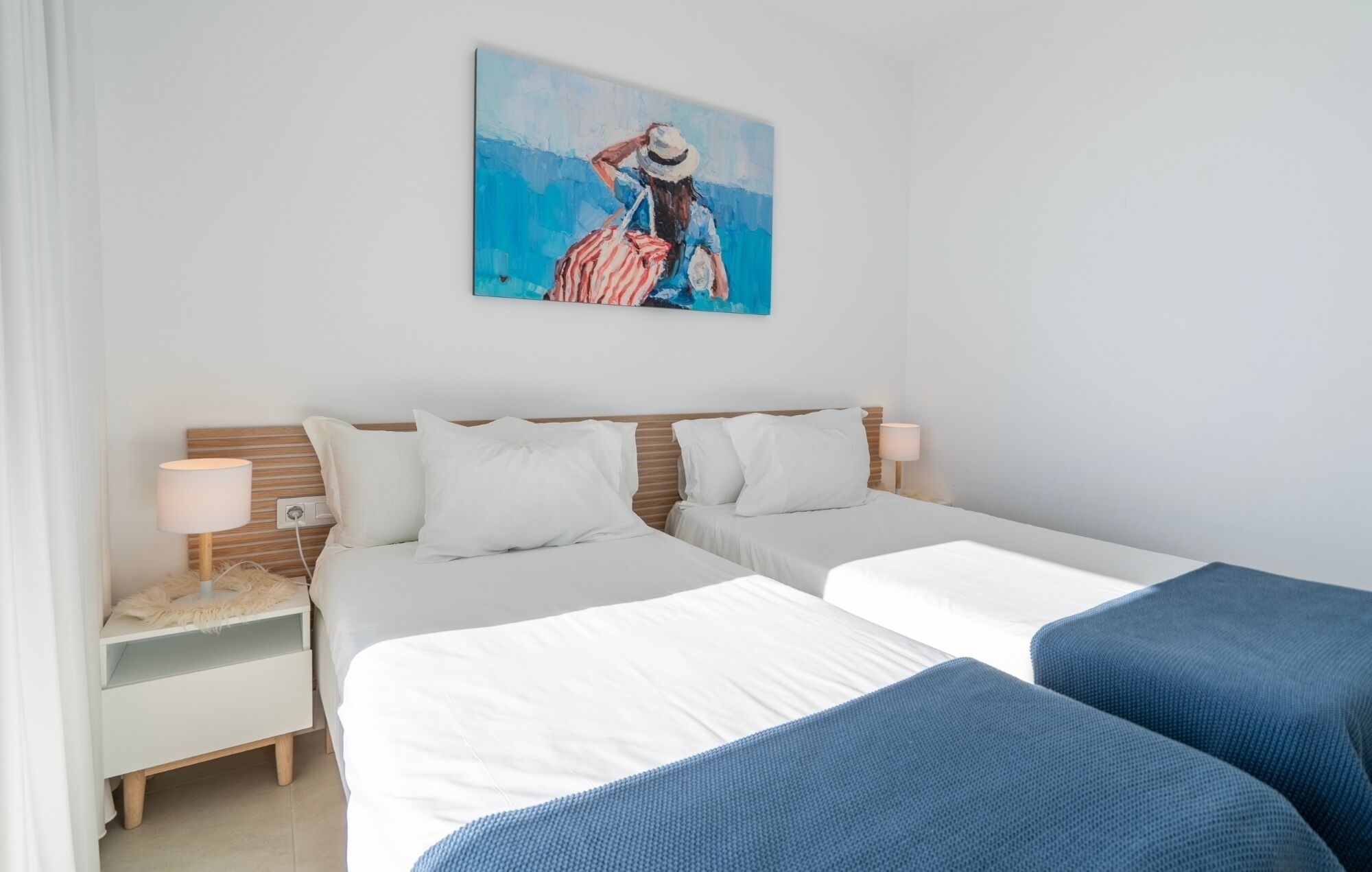 Une chambre d’hôtel avec deux lits, une table de chevet avec une lampe, un tableau au mur et une fenêtre avec des rideaux.