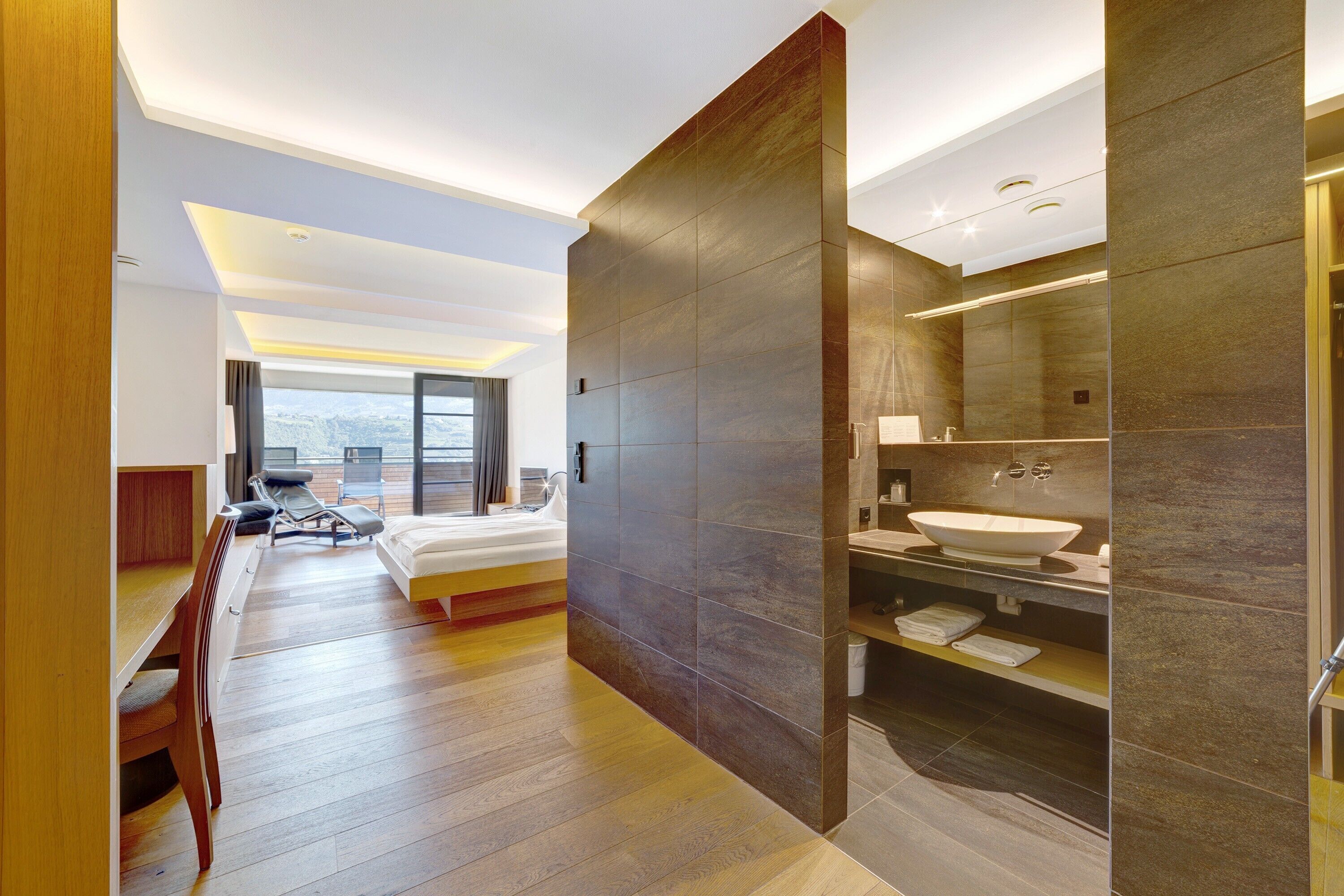 Une chambre d’hôtel moderne dotée d’un grand lit, d’un bureau, d’une chaise, d’une salle de bain avec un grand miroir et un lavabo, et offrant une vue sur la ville.