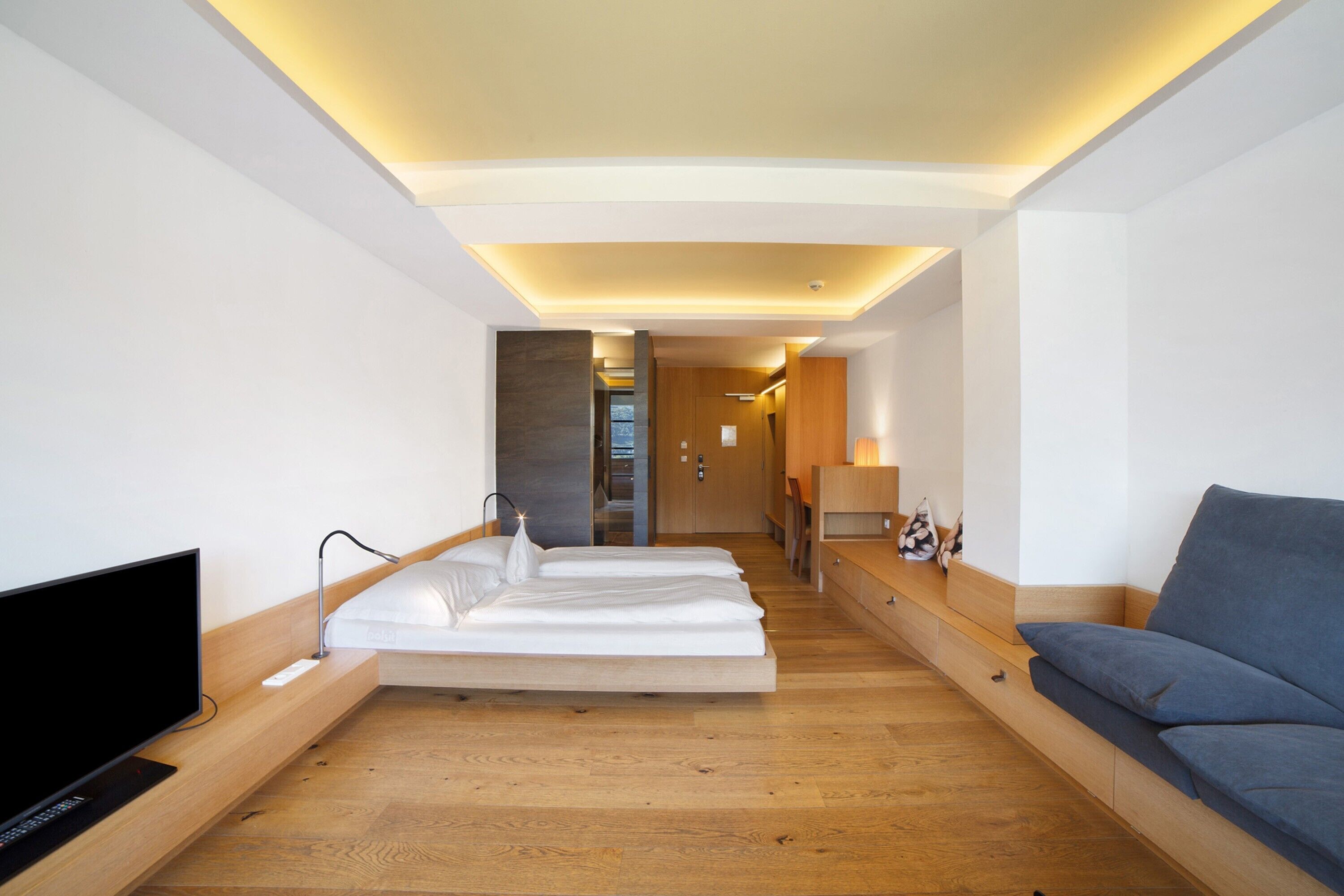 Ein Hotelzimmer mit Fernseher, zwei Betten, einer Couch, einem Schreibtisch und einer Lampe.