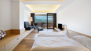 A hotel room with a bed, a seating area with a chair and a table, a TV, and a balcony with a view.