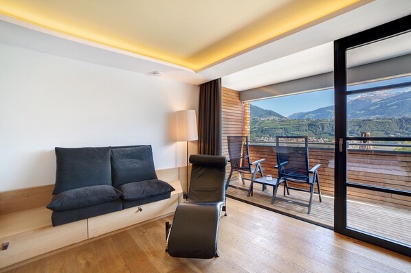 A modern room with a sofa, a reclining chair, a table, and a view of a balcony with outdoor furniture.