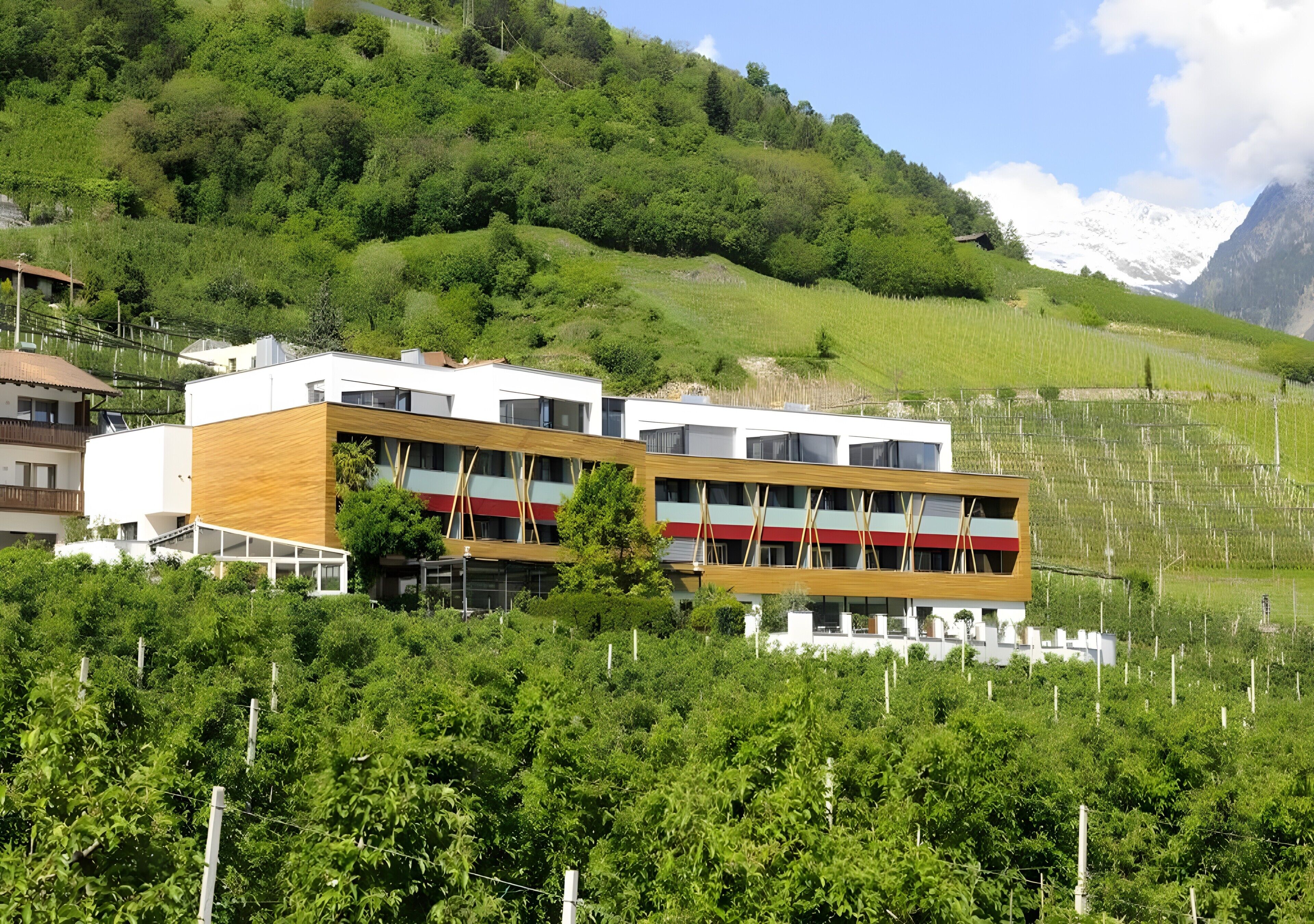 Un bâtiment moderne à plusieurs étages, entouré d’une végétation luxuriante et dominé par un paysage montagneux.