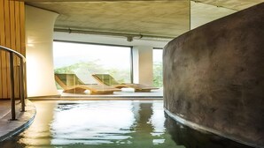 Ein Swimmingpool mit Holzterrasse und Liegestühlen, umgeben von großen Fenstern und einem Betonbau.