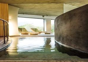 Piscina con muelle de madera y sillas de descanso, rodeada de amplias ventanas y una estructura de hormigón.