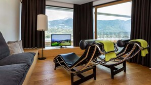 Een moderne woonkamer met een bank, een televisie en twee fauteuils, met uitzicht op de bergen.