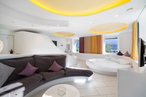 Een moderne hotelkamer met een gebogen bank, een wit bed, een flatscreen televisie en een groot raam met uitzicht.