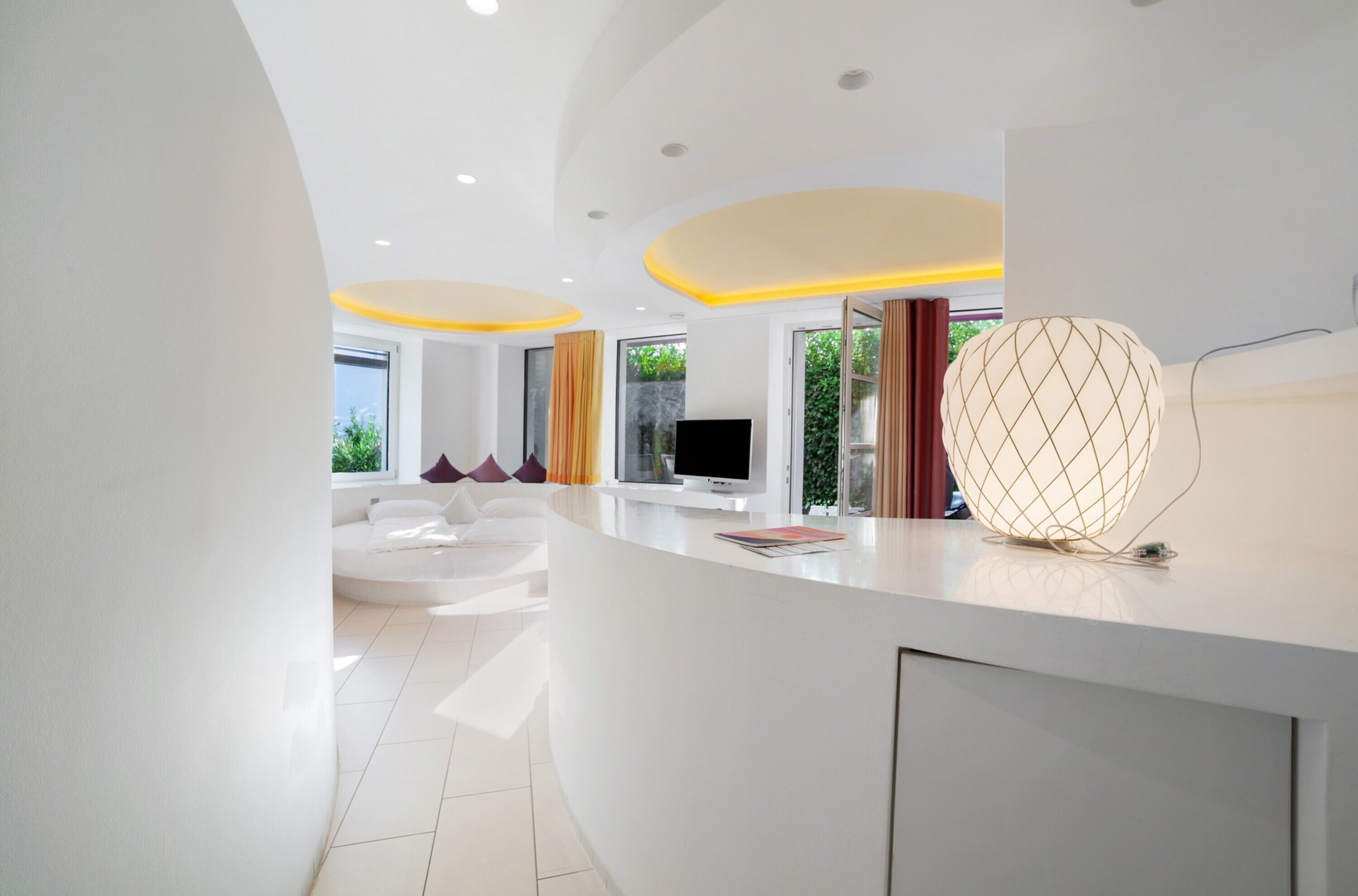 Un interno moderno con una reception dal design curvo e bianco, un televisore a schermo piatto e un'originale lampada a sfera.
