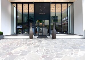 Une entrée moderne avec une façade en verre, une enseigne indiquant « PAZEIDER » et deux grands vases placés de part et d’autre.