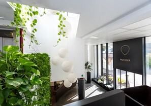 A modern interior with hanging plants, a black wall with a logo, and large windows.