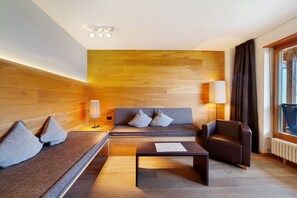 Una sala moderna con un sofá, un sillón y una mesa de centro, paneles de madera en la pared y un ventanal con cortinas.