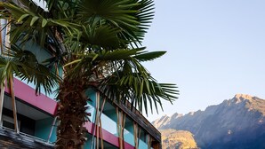 Un edificio de diseño moderno, con un balcón que tiene una palmera y montañas al fondo.