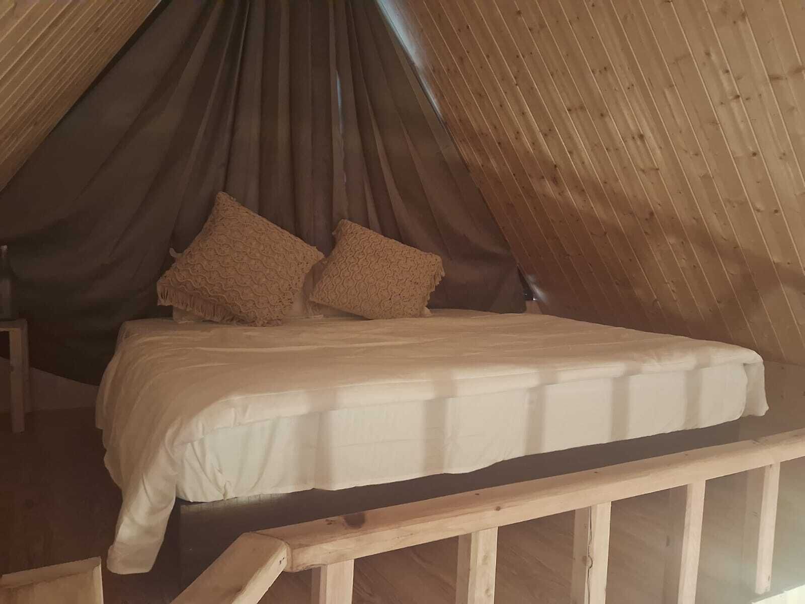 A single bed in a wooden attic room with a sloped ceiling, two pillows, and a wooden railing.