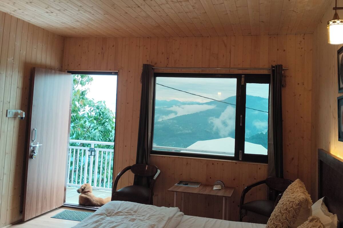 Una habitación de cabaña de madera con una cama, una ventana con vista a las montañas, una mesita y una silla.