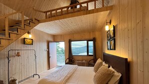 Une chambre dans une cabane en bois, avec un lit, une petite table, une chaise, une fenêtre donnant sur un paysage agréable et un escalier.