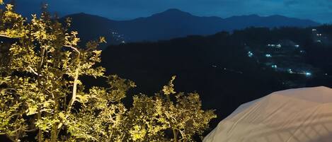 A tented outdoor area with a view of distant mountains and a tree with illuminated lights.