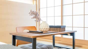 Une pièce de style japonais traditionnel, avec un sol recouvert de tatamis, une basse table en bois, un vase blanc contenant des fleurs séchées, une télécommande noire et un panier tressé.