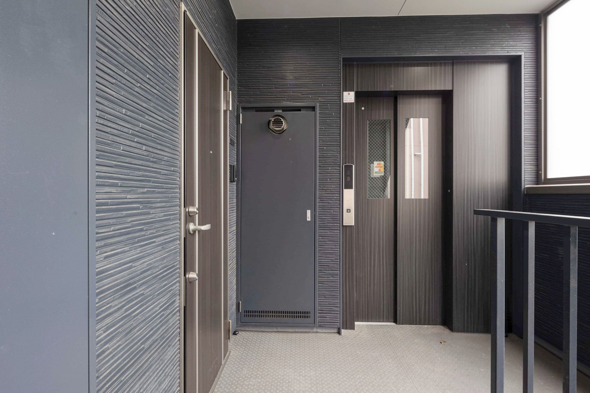 Un couloir moderne avec une porte fermée, une petite fenêtre et une rambarde en métal.