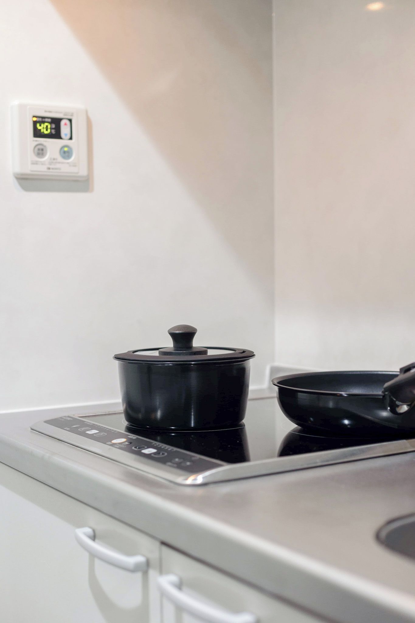 A kitchen with a stove, a pot on the stove, and a digital thermostat on the wall.