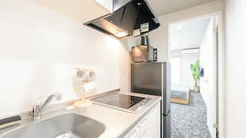 Une cuisine compacte équipée d’un évier, d’une cuisinière et d’un four à micro-ondes. On y trouve un petit plan de travail et un meuble sur lequel est posé le four à micro-ondes. Une plante est visible à l’arrière-plan.