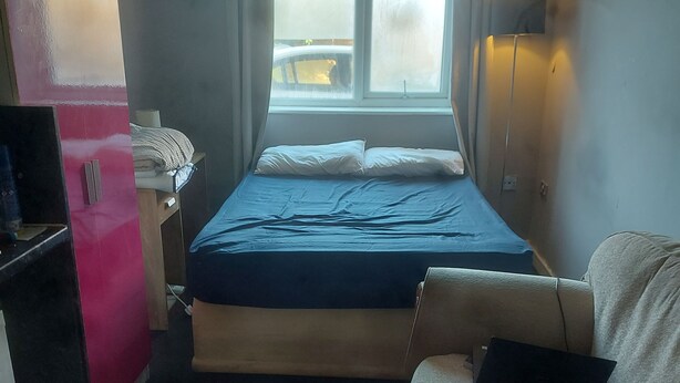 A compact hotel room with a bed, a sofa, a desk with a laptop, and a window with curtains.