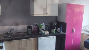 A compact kitchen with a refrigerator, a sink, and a coffee maker. There is a bag of protein powder on the counter.