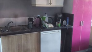 A kitchen with a sink, a coffee maker, a bag of protein powder, and a pink cabinet.