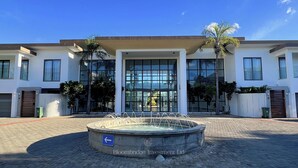 Un bâtiment moderne avec une entrée centrale, une fontaine à l’avant et une zone dallée.