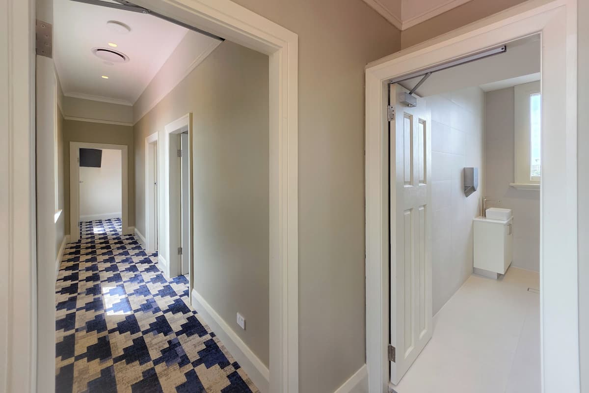 A hallway with a checkered floor leading to a bathroom with a toilet and a sink.