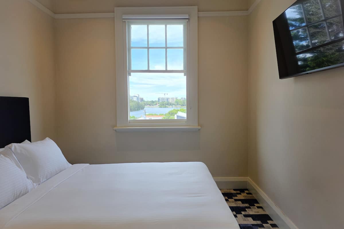 A hotel room with a bed, a window with a view of buildings and trees, and a black and white patterned floor.