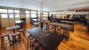 Um restaurante espaçoso com várias mesas e cadeiras de madeira, janelas amplas e um bar.