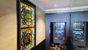 Entrada de um hotel com uma janela de vitrais com a palavra 'CIDER' e um letreiro de boas-vindas para o Hotel Riverview.