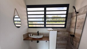 Une salle de bain moderne avec une grande fenêtre, un meuble-lavabo en bois, une douche et une petite poubelle.