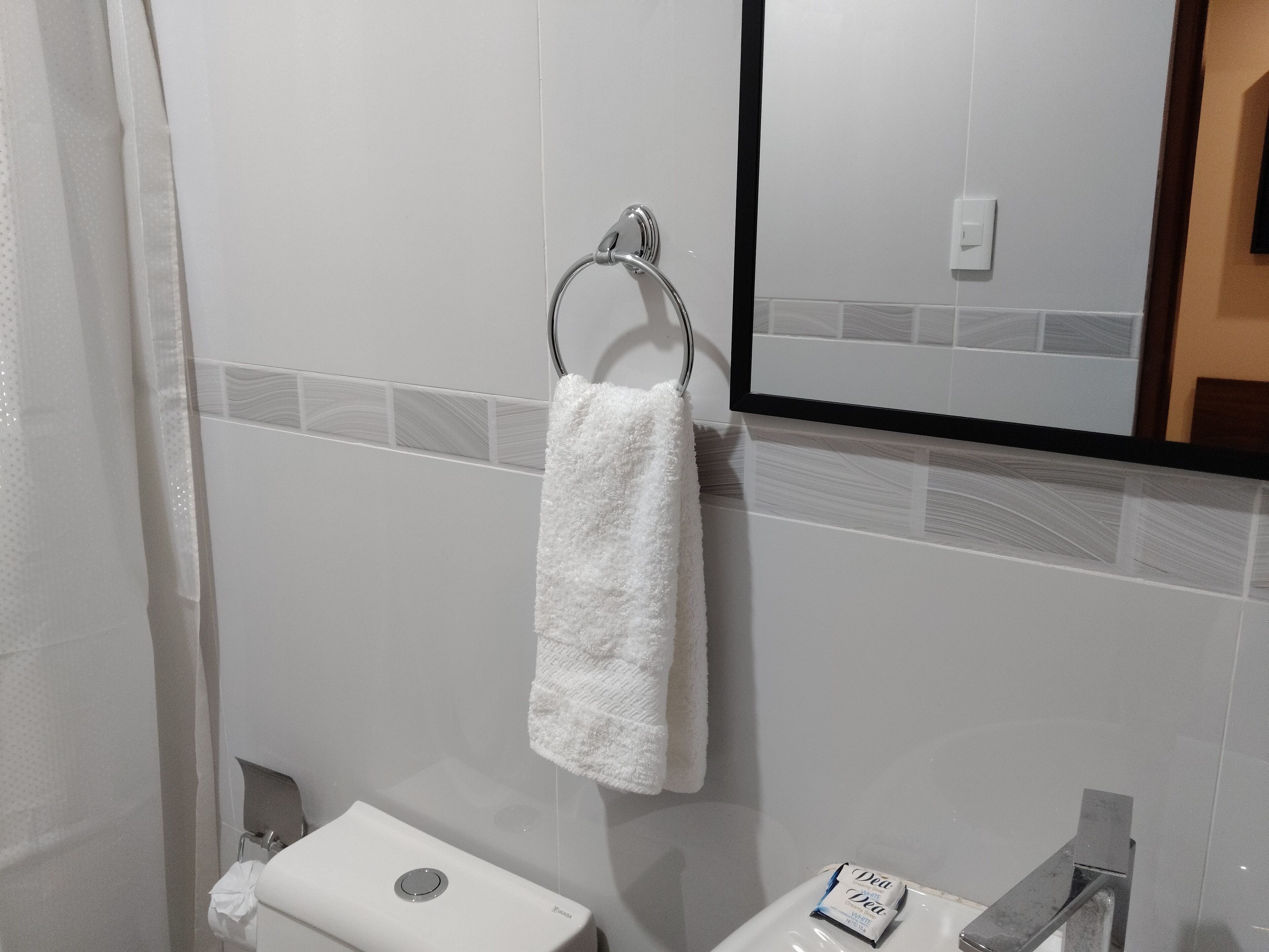 A bathroom with a white towel hanging on a metal towel ring, a white toilet, and a sink with a soap dispenser.