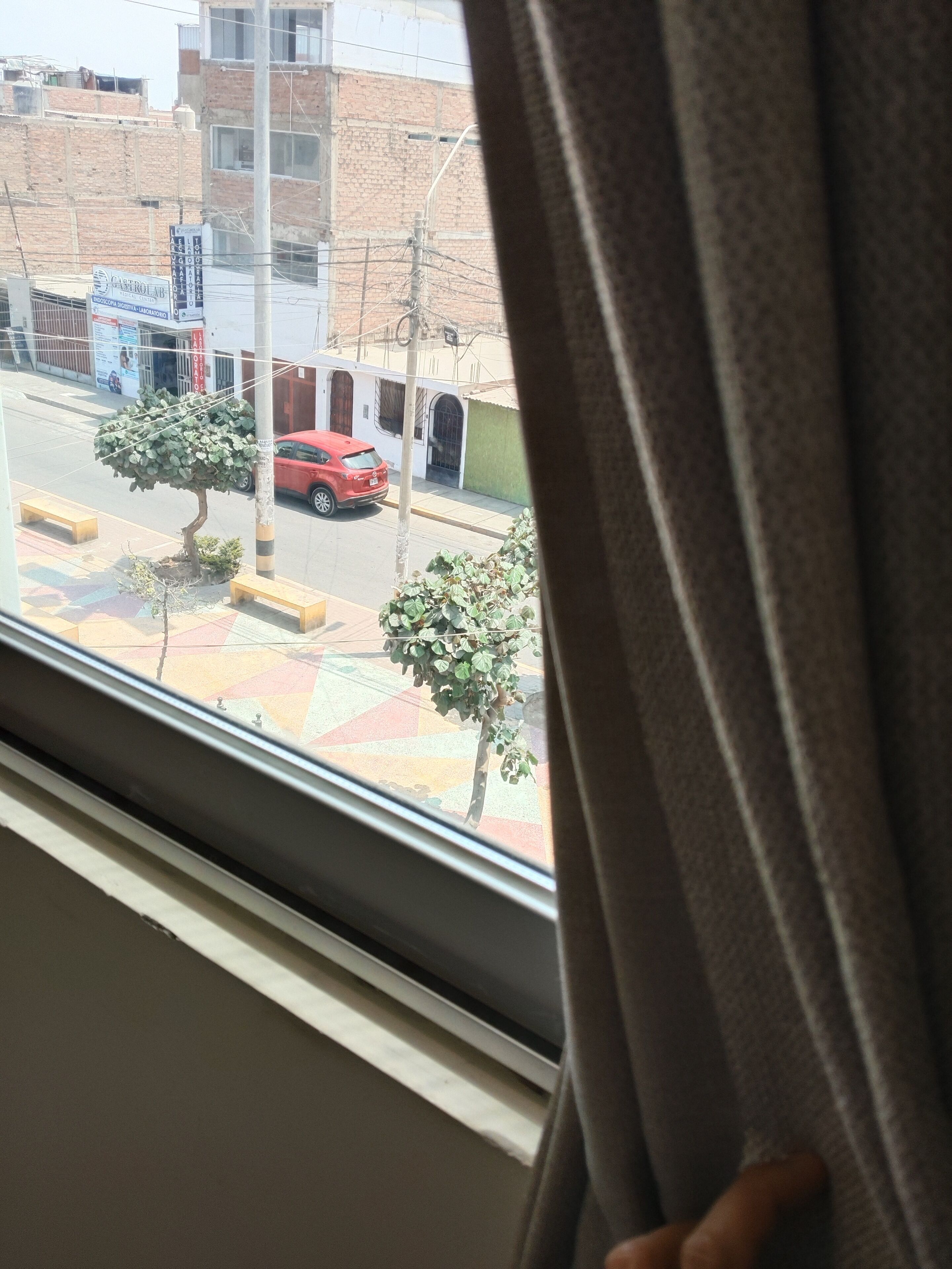 Una ventana con vista a una calle, un coche rojo y un edificio con un letrero.