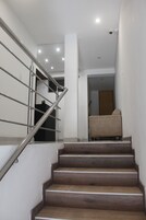 Una escalera con barandales metálicos y escalones de madera que conduce a una habitación con un sillón color beige.