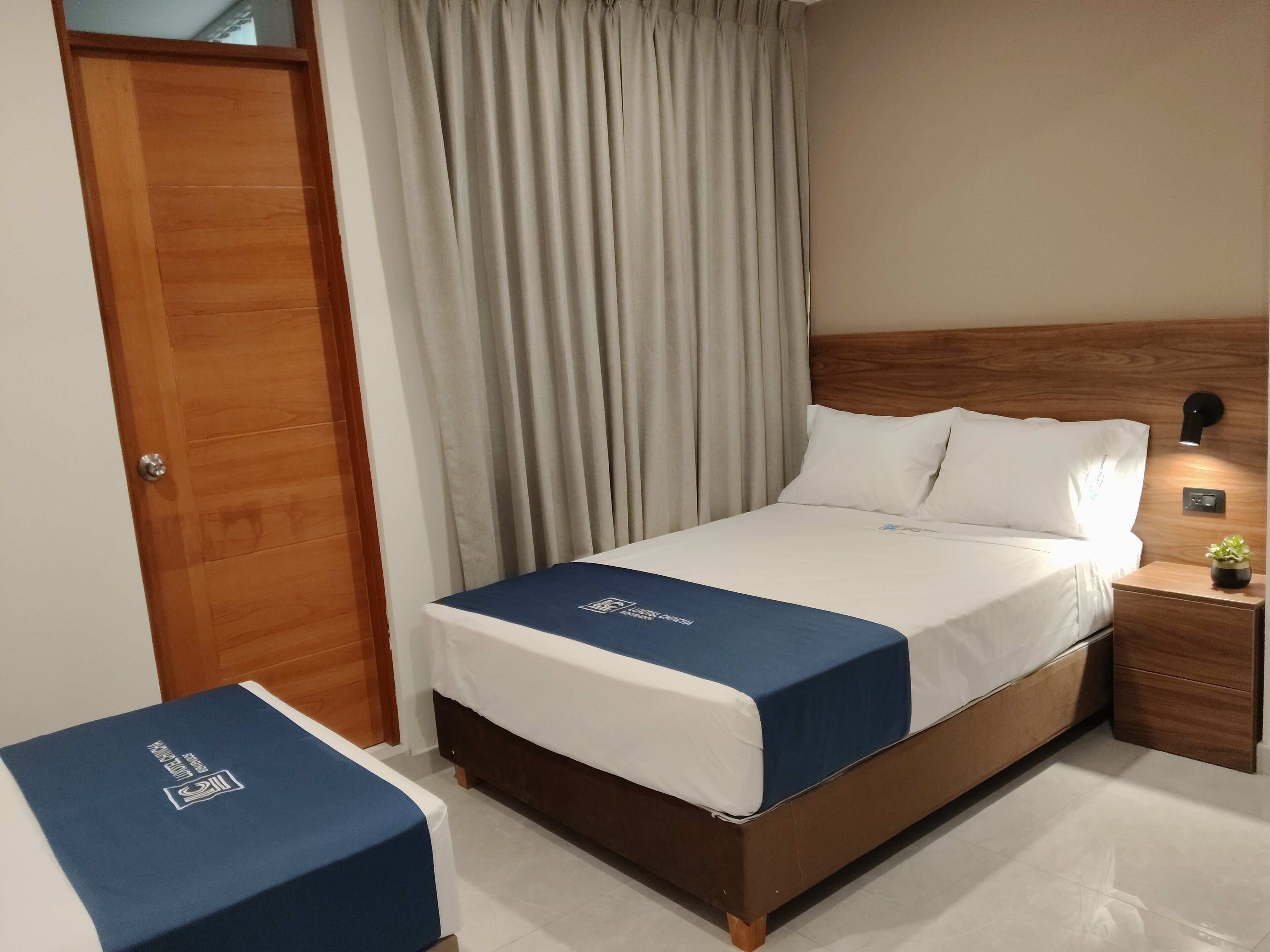 Een hotelkamer met een houten bed, een nachtkastje met een lamp en een blauw beddekleed.