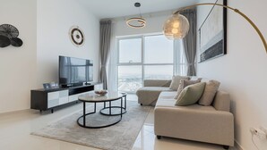 Ein modernes Wohnzimmer mit Flachbildfernseher, Couchtisch, Sofa und einem großen Fenster mit Blick auf die Stadt.