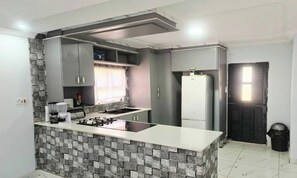 A compact kitchen with a central island, built-in appliances, and a tiled backsplash. - Raneziah Guesthouse (Kasane)
