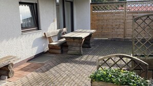 A patio with a wooden table and benches, a small garden bed with plants, and a wooden fence. - Vacation apartment in Starnberg, close to the lake and town (Starnberg)