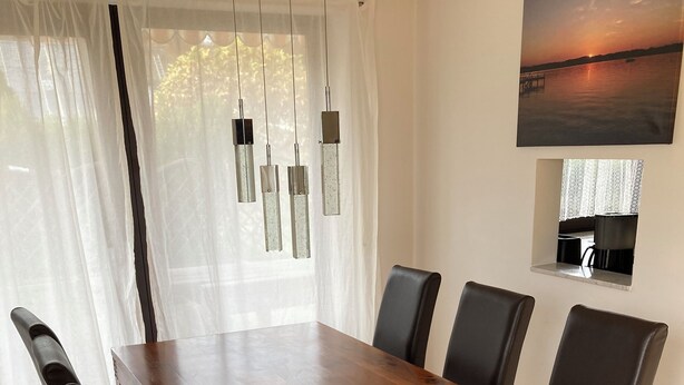 A dining area with a wooden table and black chairs, a window with sheer curtains, and a painting on the wall. - Vacation apartment in Starnberg, close to the lake and town (Starnberg)