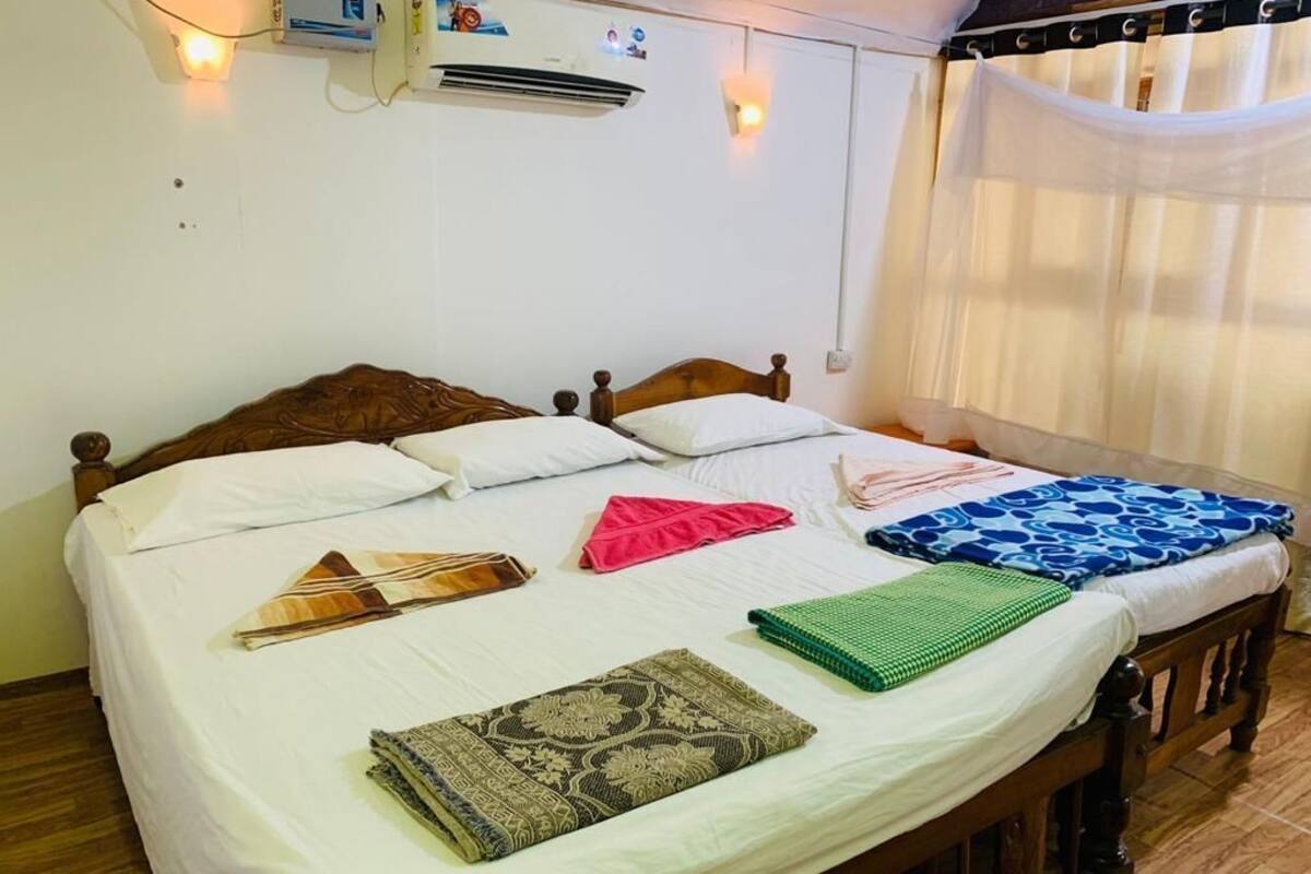 A bed with a wooden headboard, white linens, and several folded blankets and pillows.