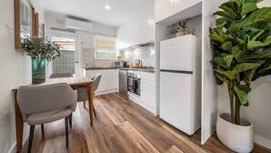 Une cuisine moderne avec des meubles blancs, une table à manger en bois et une grande plante en pot.