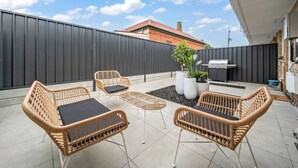 Une terrasse avec des meubles en osier, un barbecue et des plantes en pot.