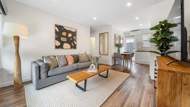 Un salon moderne avec un canapé gris, une table basse en bois et un grand téléviseur posé sur un meuble en bois.