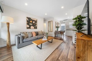 A modern living room with a grey sofa, wooden coffee table, and a large TV on a wooden stand. - Three Tea House — Relaxed Living in Mile End (Mile End)