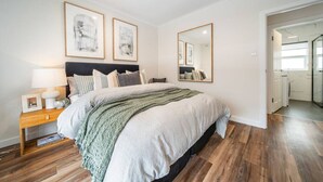 Une chambre à coucher moderne avec un grand lit, des tables de chevet, un miroir et des œuvres d’art encadrées accrochées au mur.
