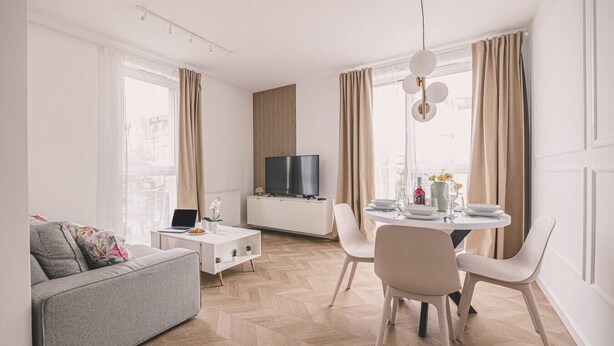 Una sala moderna con un sofá gris, una mesa de comedor para cuatro personas y un televisor sobre un mueble blanco.
